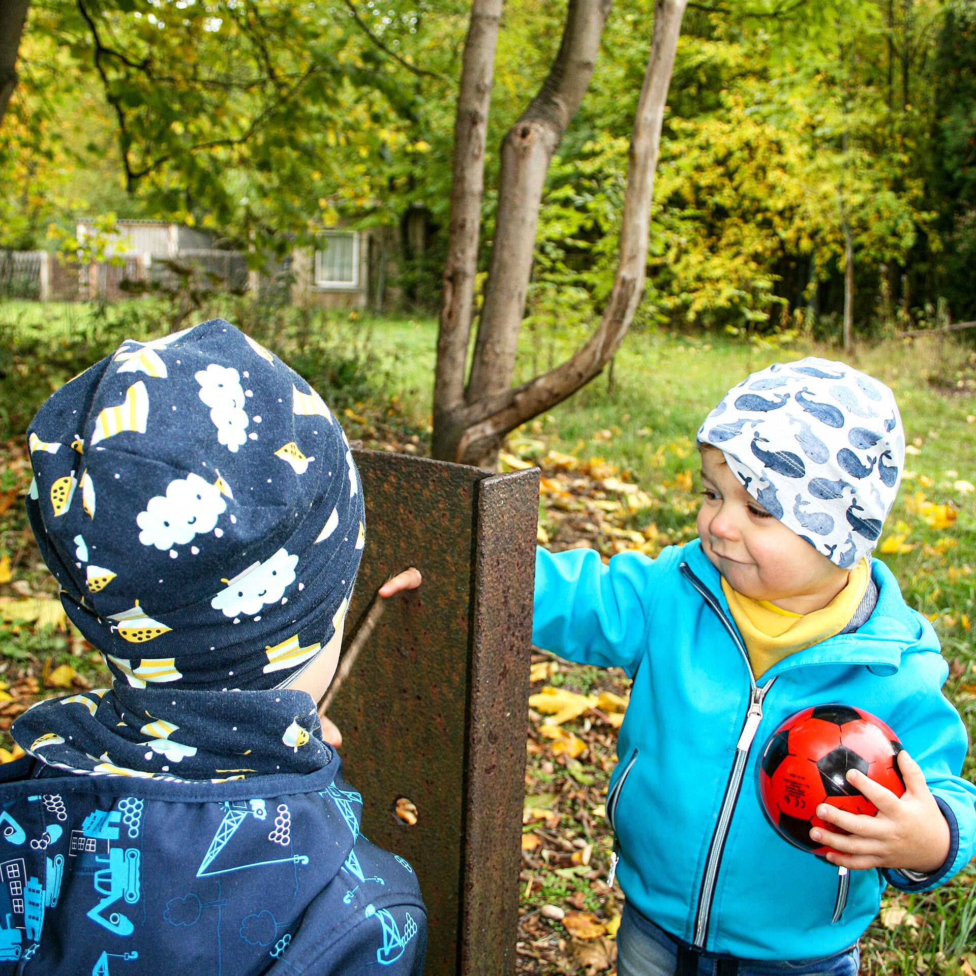 Zwei Kinder spielen im Freien auf einer Wiese an einem Baum.