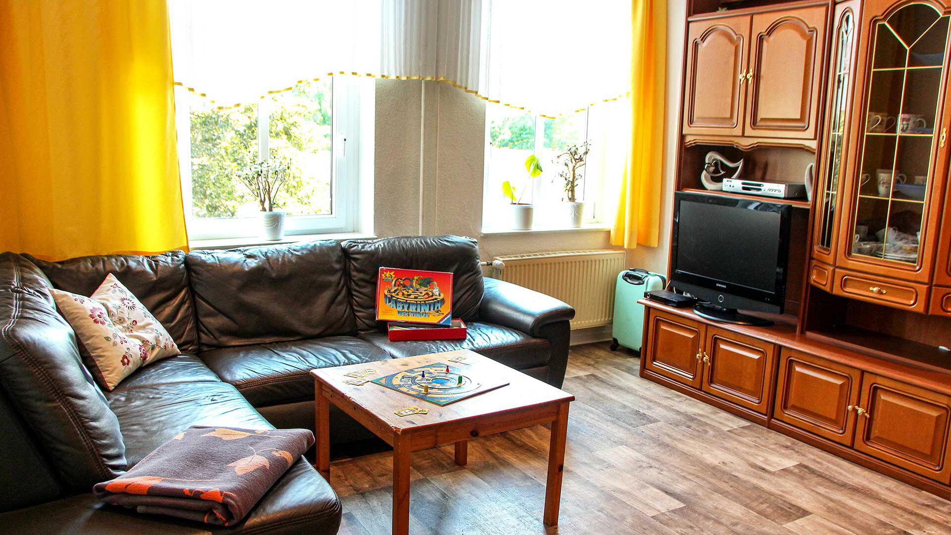 Ein Gruppenraum mit einem Ecksofa, Sofatisch, einer Anbauwand und einem Fernseher.