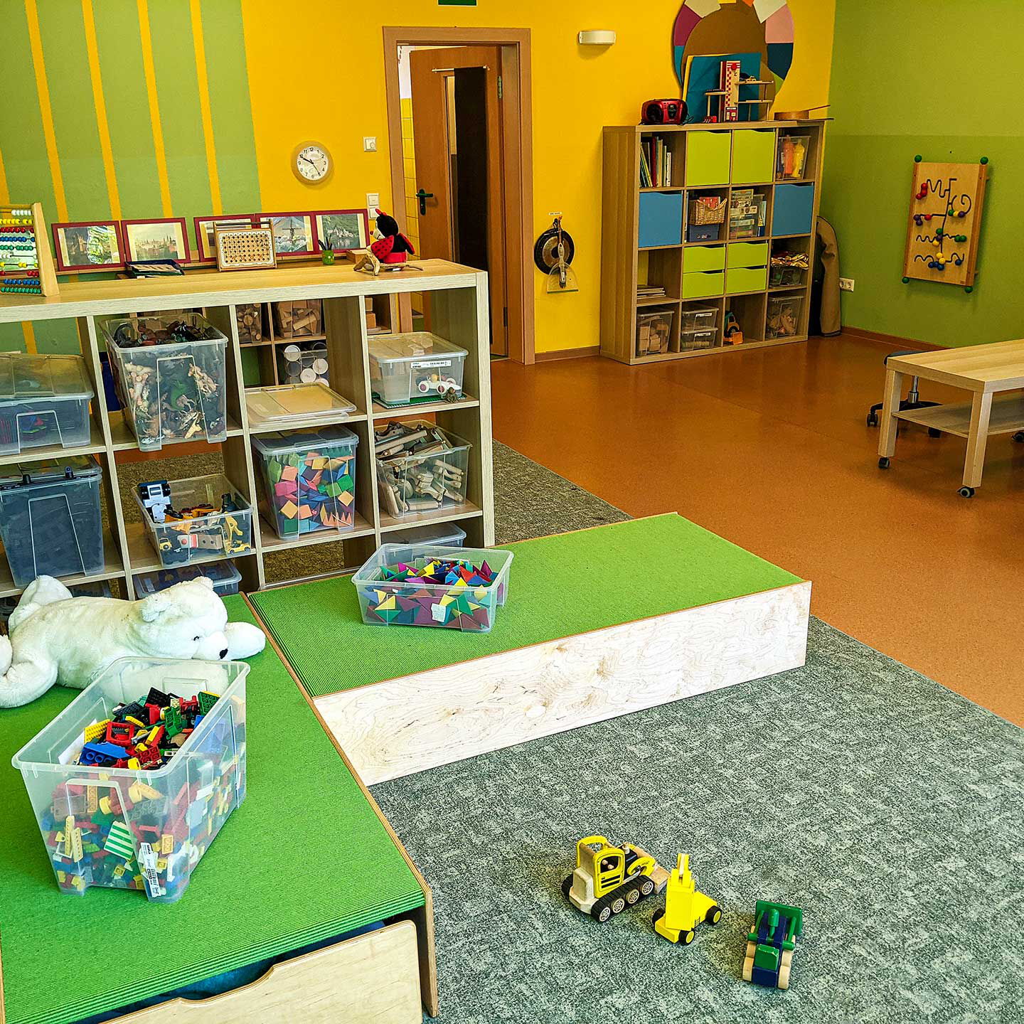 Das Bauzimmer der Kita mit unterschiedlichen Spielzeug, Spielteppichen und Regalen.