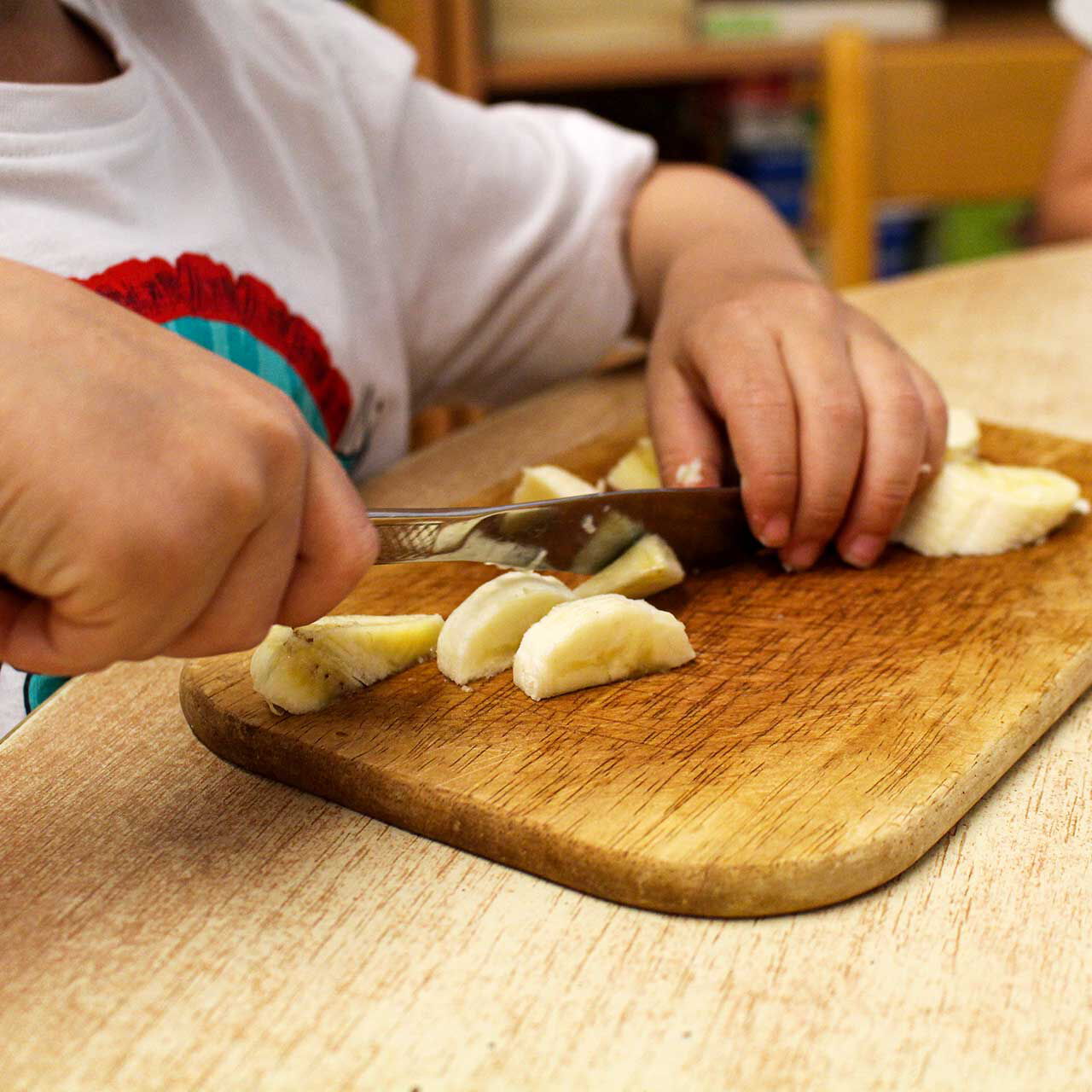 Ein Kleinkind schneidet mit einem Messer eine Banane in Stücke.