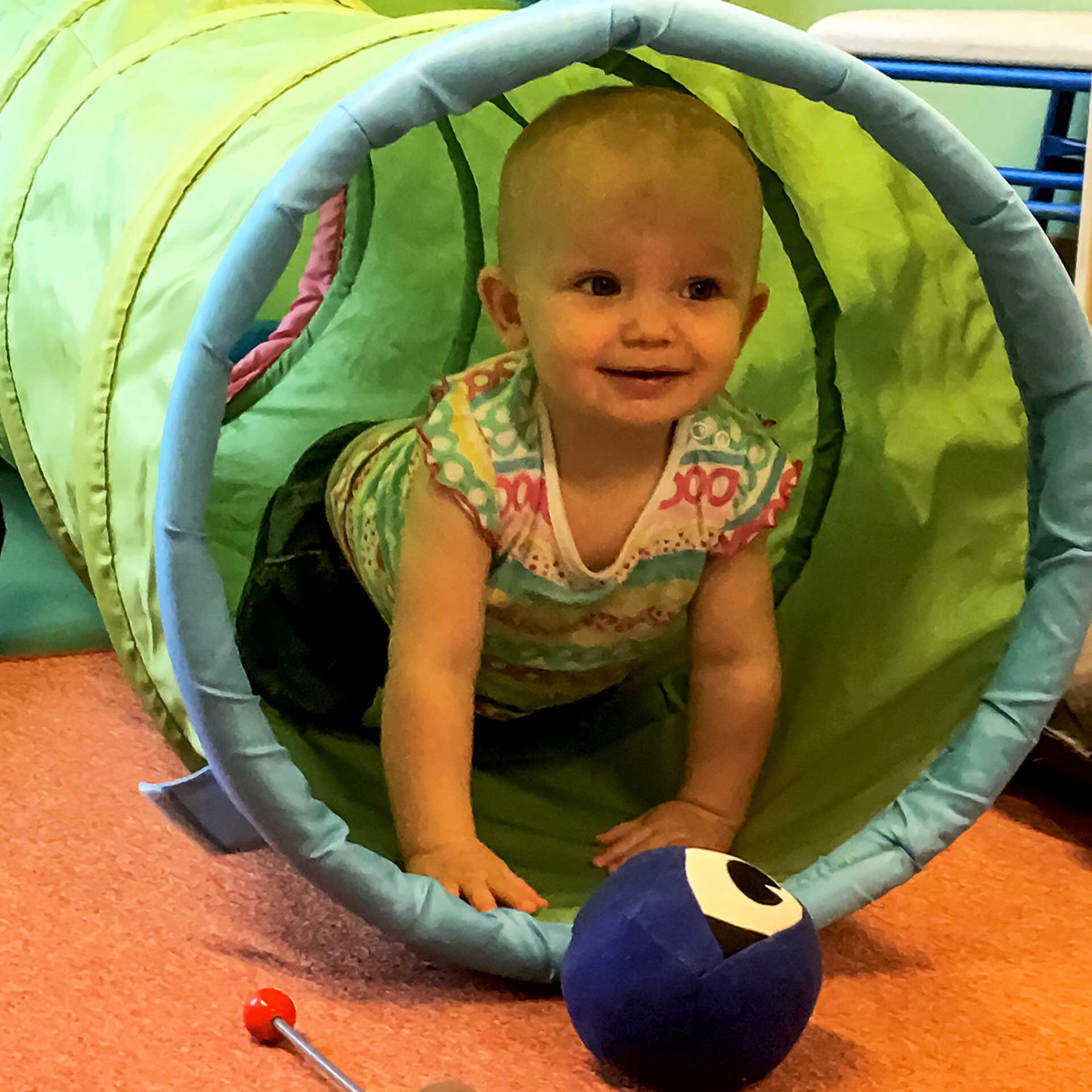 Ein Kleinkind krabbelt in einer Röhre und spielt nebenbei mit einem kleinen Stoffball.