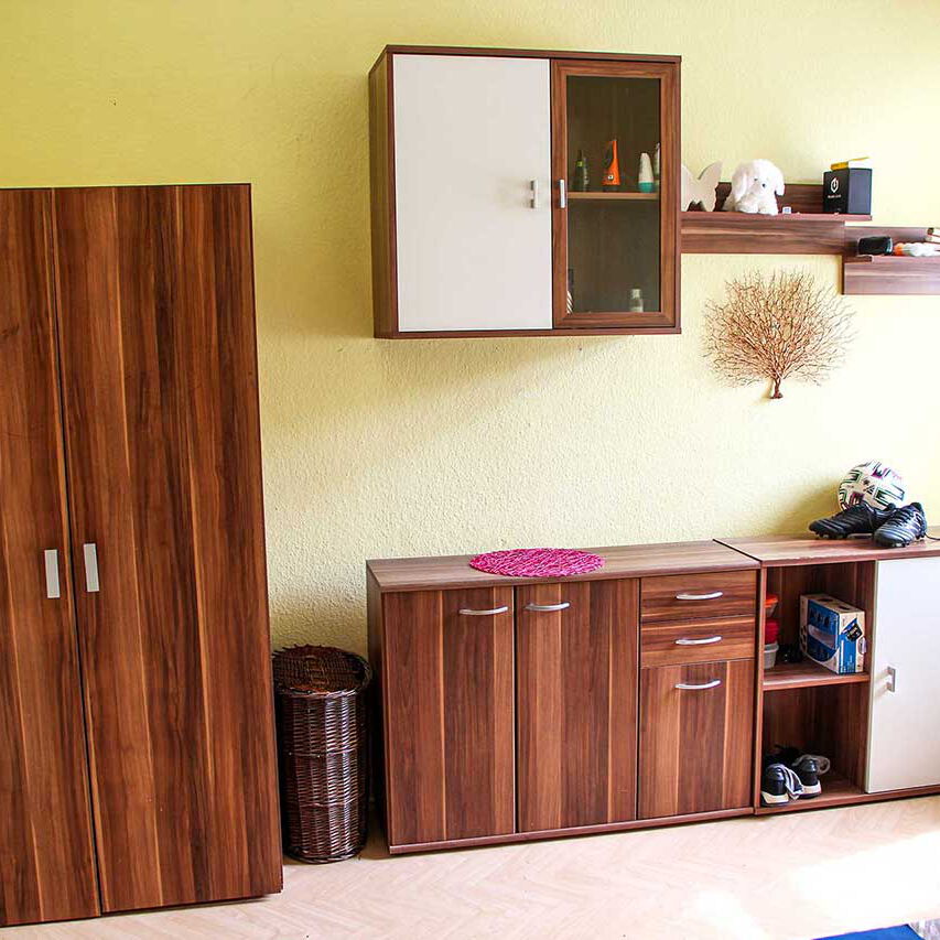 Ein Wohnbereich mit einem Kleiderschrank, zwei Kommoden, einem Hängeschrank und Wandboard.