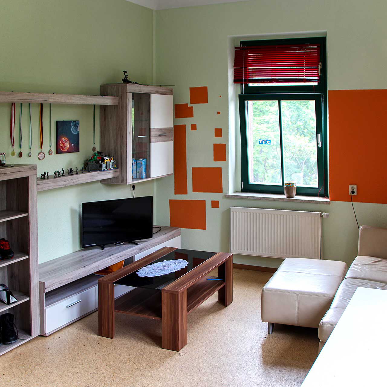 Eine Wohnlandschaft in einem Jugendzimmer mit einem Ledersofa, Sofatisch und einer Anbauwand mit TV.