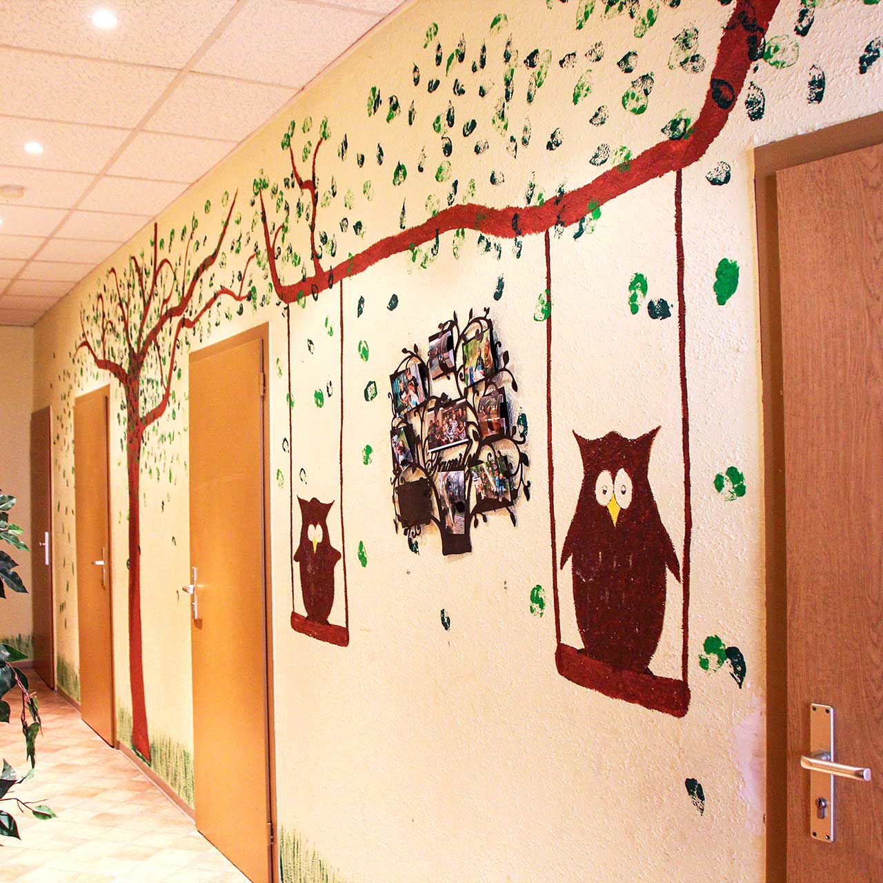 Der Flurbereich mit fünf Eingangstüren in die jeweiligen Zimmer. Die Wand ist mit einem Baum, Blättern, Schaukeln und Eulen bemalt.