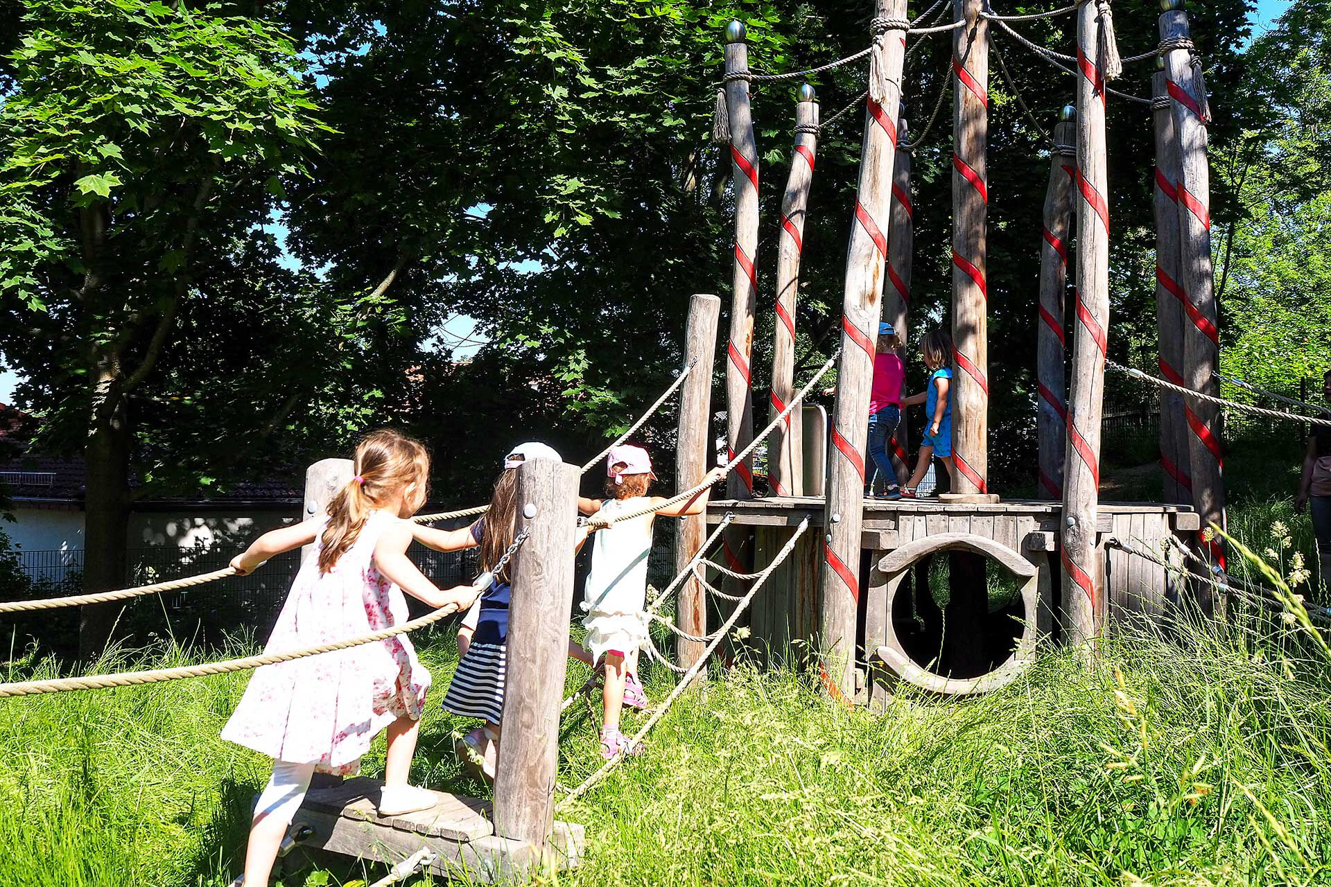 Auf dem Kletterbaum aus Holz spielen und klettern fünf Kleinkinder.