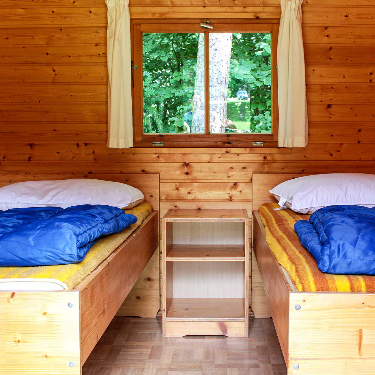 Der Innenbereich eines Holzhäuschen mit zwei Einzelbetten und einem Nachttischschrank.