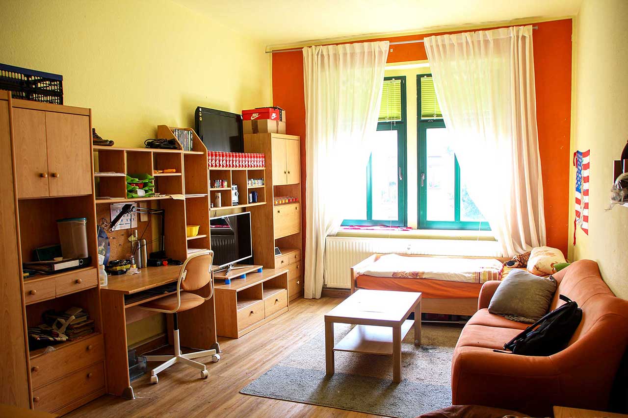 Ein großes Jugendzimmer mit einer Anbauwand, einem Sofa, Bett und TV. In der Anbauwand ist ein Schreibtisch integriert.